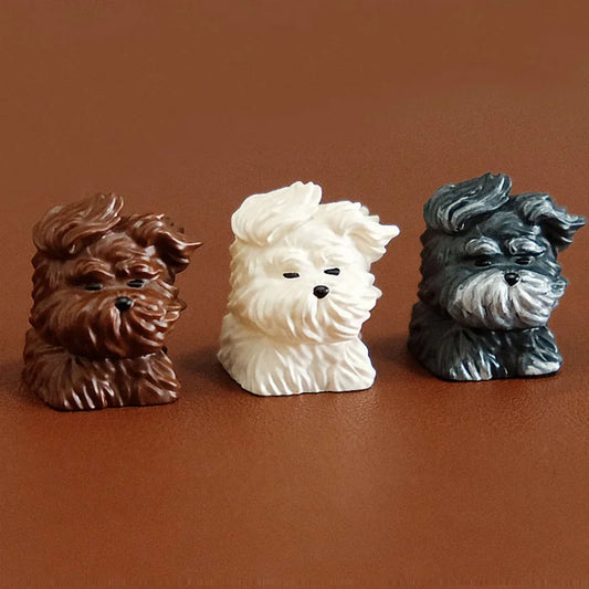 Three artisan keycaps shaped like long-haired dogs with flowing fur in chestnut brown, vanilla white, and steel-blue colors for mechanical keyboards